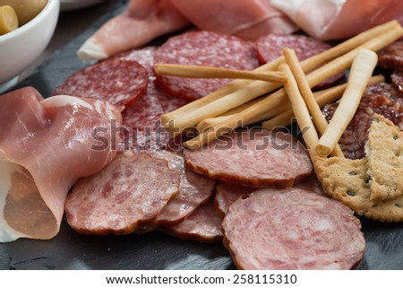 Assorted meat snacks, sausages on a blackboard, close-up, horizontal