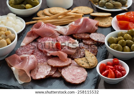 Assorted deli meat snacks, sausages and pickles on a blackboard, horizontal