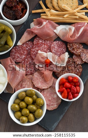 Assorted deli meat snacks, sausages and pickles on a blackboard, close-up, top view, vertical