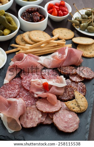 Assorted deli meat snacks, sausages and pickles on a blackboard, vertical, top view
