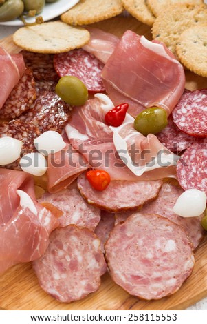 Assorted deli meat snacks, sausages and pickles on board, vertical, close-up, top view