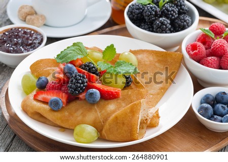 breakfast - crepes with fresh berries and honey, coffee on wooden background, close-up, horizontal