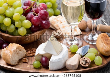 Camembert, fresh baguette, grapes, walnuts and wine on a wooden tray, close-up