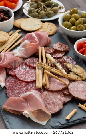 Assorted meat snacks, sausages and pickles on a blackboard, vertical, top view