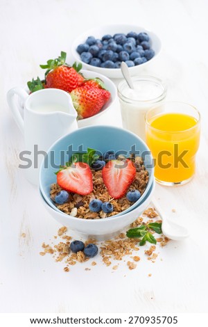 healthy breakfast - granola, fresh berries, orange juice and milk on white table, vertical