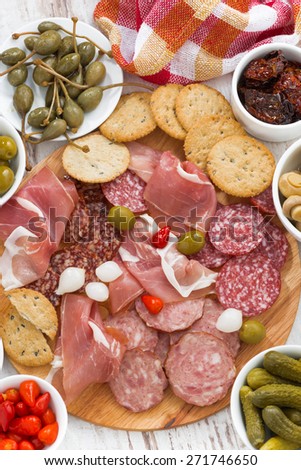 Assorted deli meat snacks, sausages and pickles on board, top view, vertical, close-up