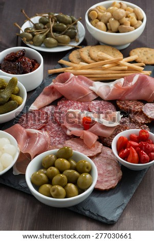 deli meat snacks, sausages and pickles on a dark wooden table, vertical, top view