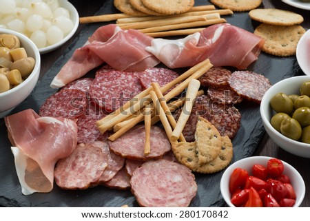 Assorted meat snacks, sausages and pickles on a blackboard, horizontal, top view