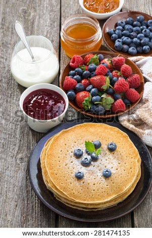 crepes, fresh berries and jams on wooden table, vertical, top view