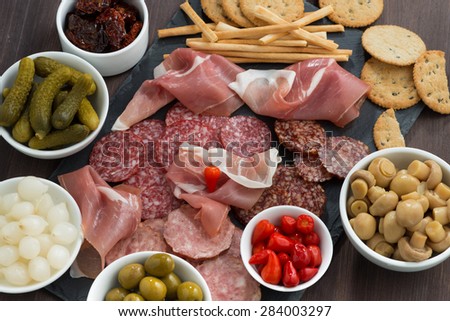 deli meat snacks, sausages and pickles on a blackboard, close-up, top view, horizontal