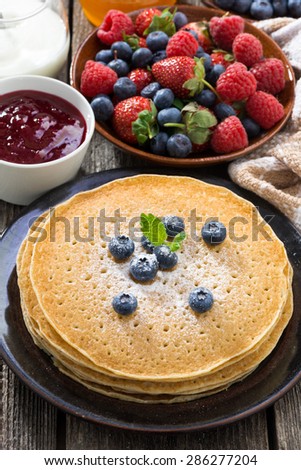 crepes, fresh berries and jams on wooden table, vertical, top view, close-up