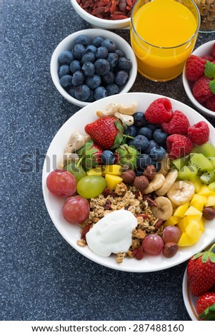 foods for a healthy breakfast - fresh berries, fruits, nuts and muesli on dark background, vertical, top view