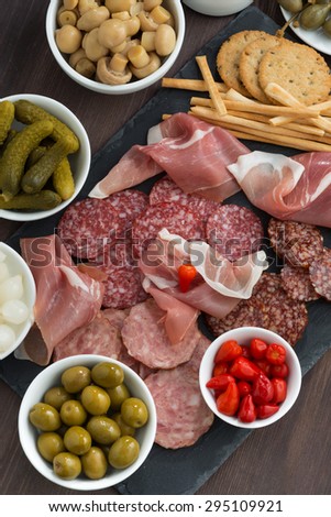 Assorted deli meat snacks, sausages and pickles on a blackboard, top view, vertical