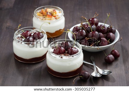 dessert with cream and jam in glass jar on wooden table, closeup
