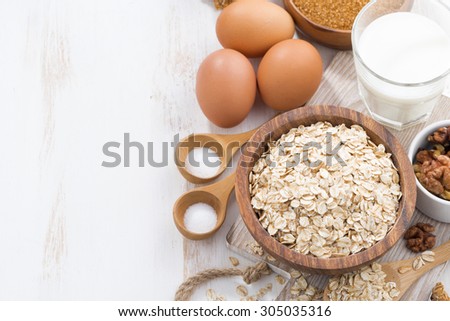oat flakes and ingredients for making cookies on white wooden table, top view, horizontal