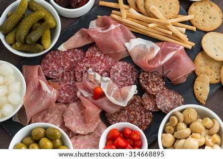 deli meat snacks, sausages and pickles on a blackboard, top view, horizontal