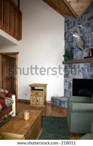 The interior of a rustic cabin showing a stone fireplace, stag;s head, and lot\'s of wood