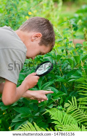 portrait of the boy in a garden, considers plants through a magnifying glass