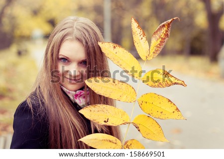 Portrait of the attractive young woman with an autumn leaf in hands against the nature of fall