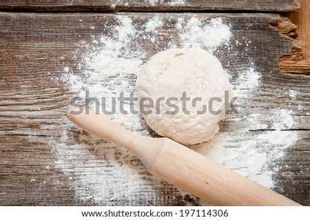 Classic wooden rolling pin with freshly prepared dough and dusting of flour on wooden background