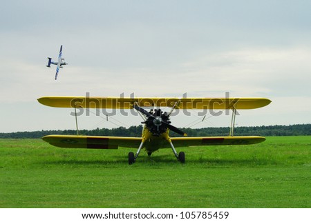small aeroplane standing on a grass, small aeroplane flying in the background, during yearly air meetings, Masuria, Poland