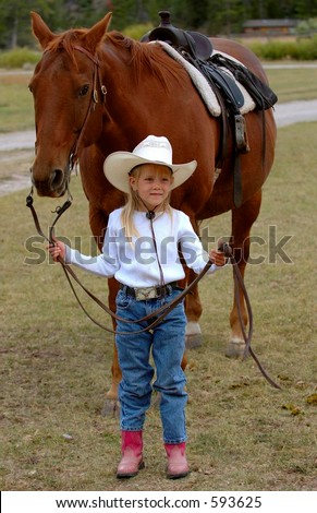 Little cowgirl holding reins of horse standing behind her