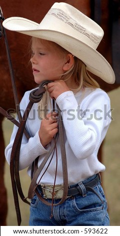 Little cowgirl adjusting her hat while holding horse reins