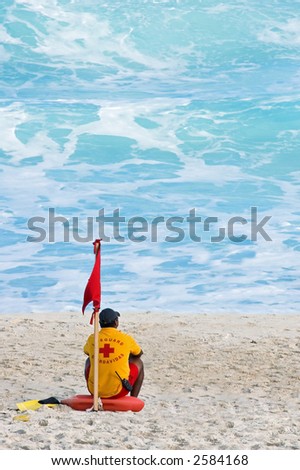 Mexican lifeguard sits on Caribbean beach next to red warning flag