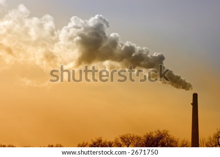 Smokestack sends up smoke against blue and orange sky