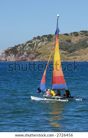 Two women and their guide set sail in a brightly colored catamaran sailboat - reflection in waves of ocean near Mazatlan Mexico