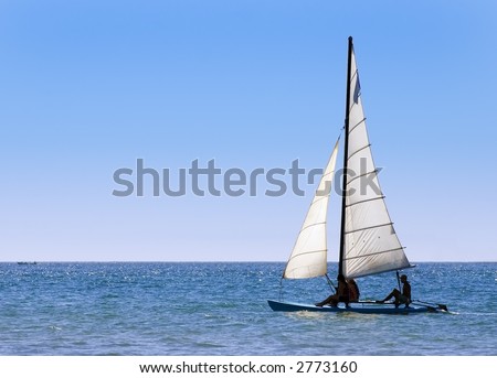 Two women and man sail catamaran sailboat out into Pacific Ocean