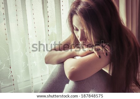 young sad woman sit beside window with vintage filter effect