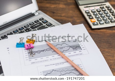 document, pencil and clips over laptop with calculator on wooden table.
