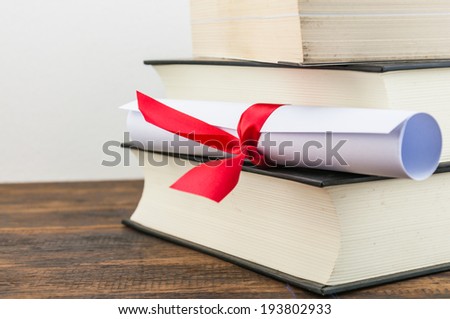A parchment diploma scroll, rolled up with red ribbon on stack of book on wood background