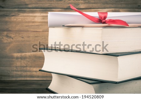 A parchment diploma scroll, rolled up with red ribbon on stack of book on wood background with vintage filter