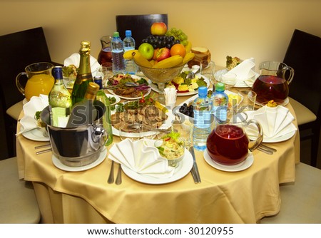 Round table with drinks, appetizers, salads, a boiled pork and fruit.