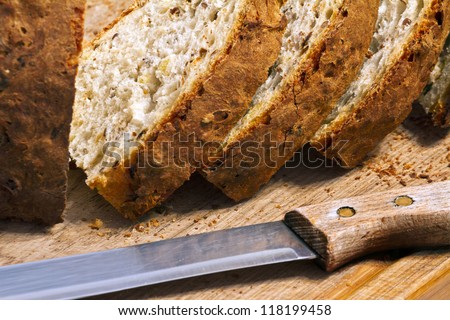 bread crumbs, a knife and a few loaves of fresh bread with a crispy crust on a wooden board
