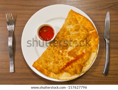 hot fried cheburek with meat and red sauce on a white plate, fork and knife