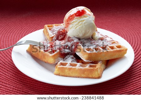freshly baked Belgian waffles with ice cream and strawberry jam in a white plate with a metal fork on a red table