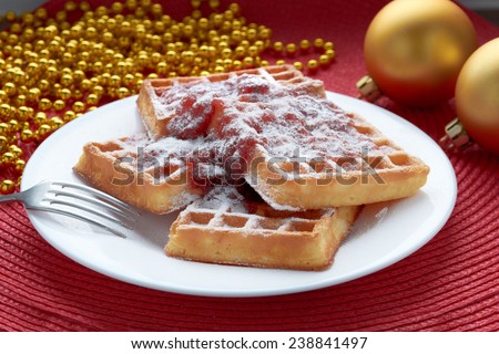 freshly baked Belgian waffles with strawberry jam in a white plate with a metal fork on a red table with golden balls