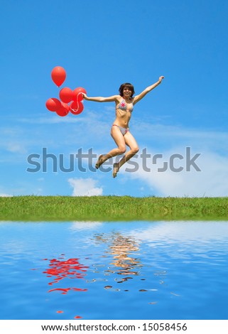 Beautiful lady in bikini with red balls jumping over  lake
