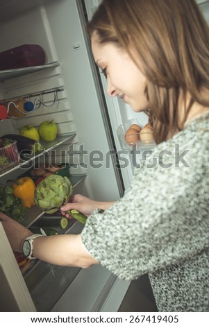Young woman takes fruits and vegetables from the fridge out