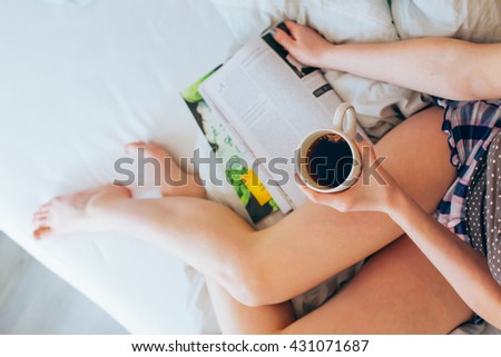Young woman lying in bed reading magazine