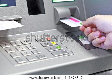 Hand inserting ATM credit card into bank machine to withdraw money