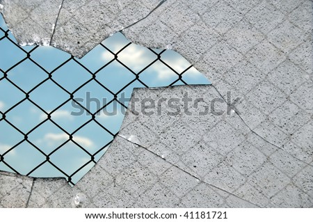Broken glass fragments and chain link wired fence pattern against blue sky.