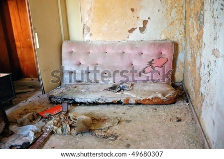 Broken couch and peeling paint wall. Abandoned house interior.