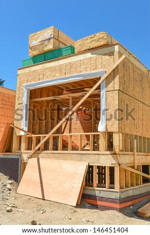 A single family home under construction. The house has been framed and covered in plywood. Stacks of 2x4 boards on the top.