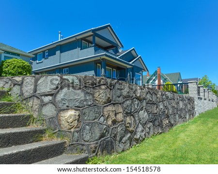Stone wall of terrace land with concrete stairs in front of a house. North American house on a blue sky background.