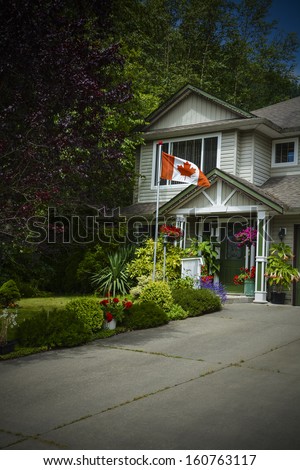 Entrance of a house with Canadian flag on front yard  in British Columbia, Canada. Entrance of a house with concrete driveway. Image darkened on the corners.