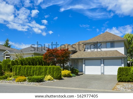 Family house with landscaping on the front and blue sky background. House with two gates garage.